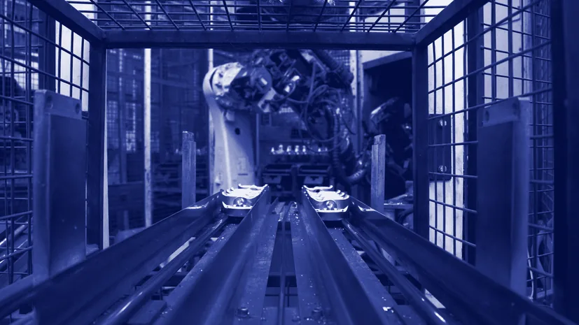 Güvenlik kafesinin arkasında, bir konveyörde çalışan robot kol